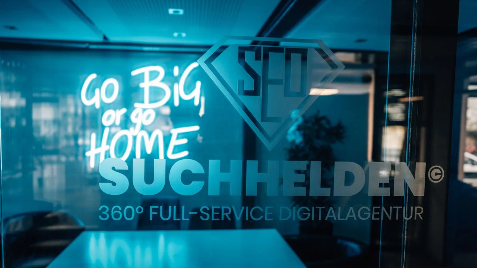Beleuchteter Suchhelden-Schriftzug „Go big or go home“ an der Glaswand in Osnabrück