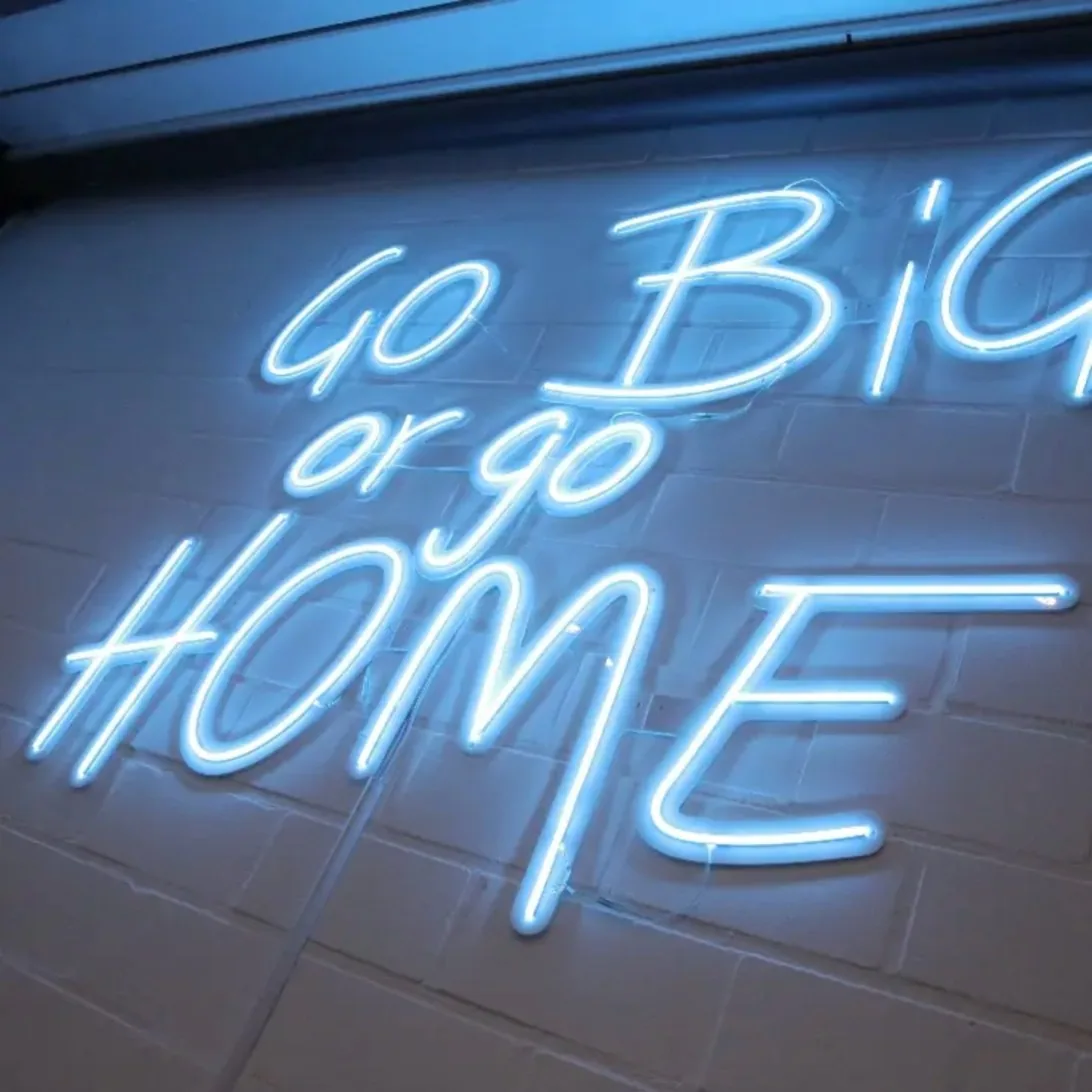 Leuchtstoffröhre an Wand zeigt Text "Go Big or Go Home" in modernem Büroumfeld Leuchtstoffröhre an Wand zeigt Text "Go Big or Go Home" in modernem Büroumfeld