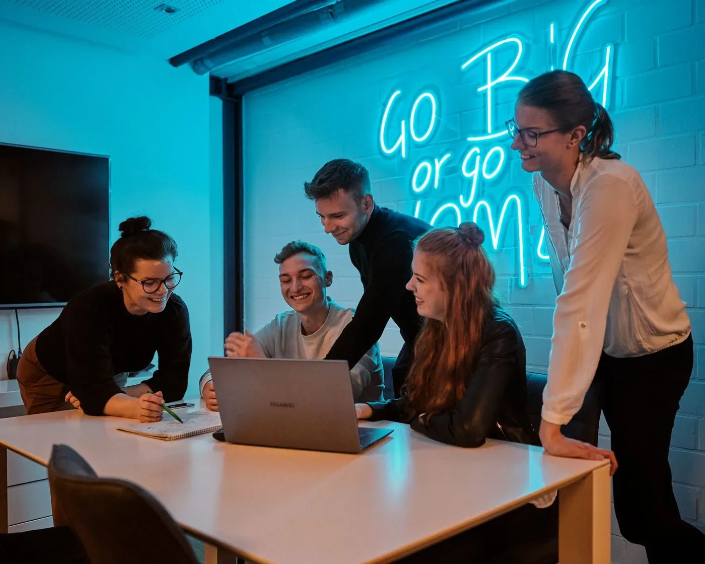 Suchhelden-Team bespricht ein Projekt am Laptop vor dem Neonschriftzug „Go big or go home“ in… Suchhelden-Team bespricht ein Projekt am Laptop vor dem Neonschriftzug „Go big or go home“ in…