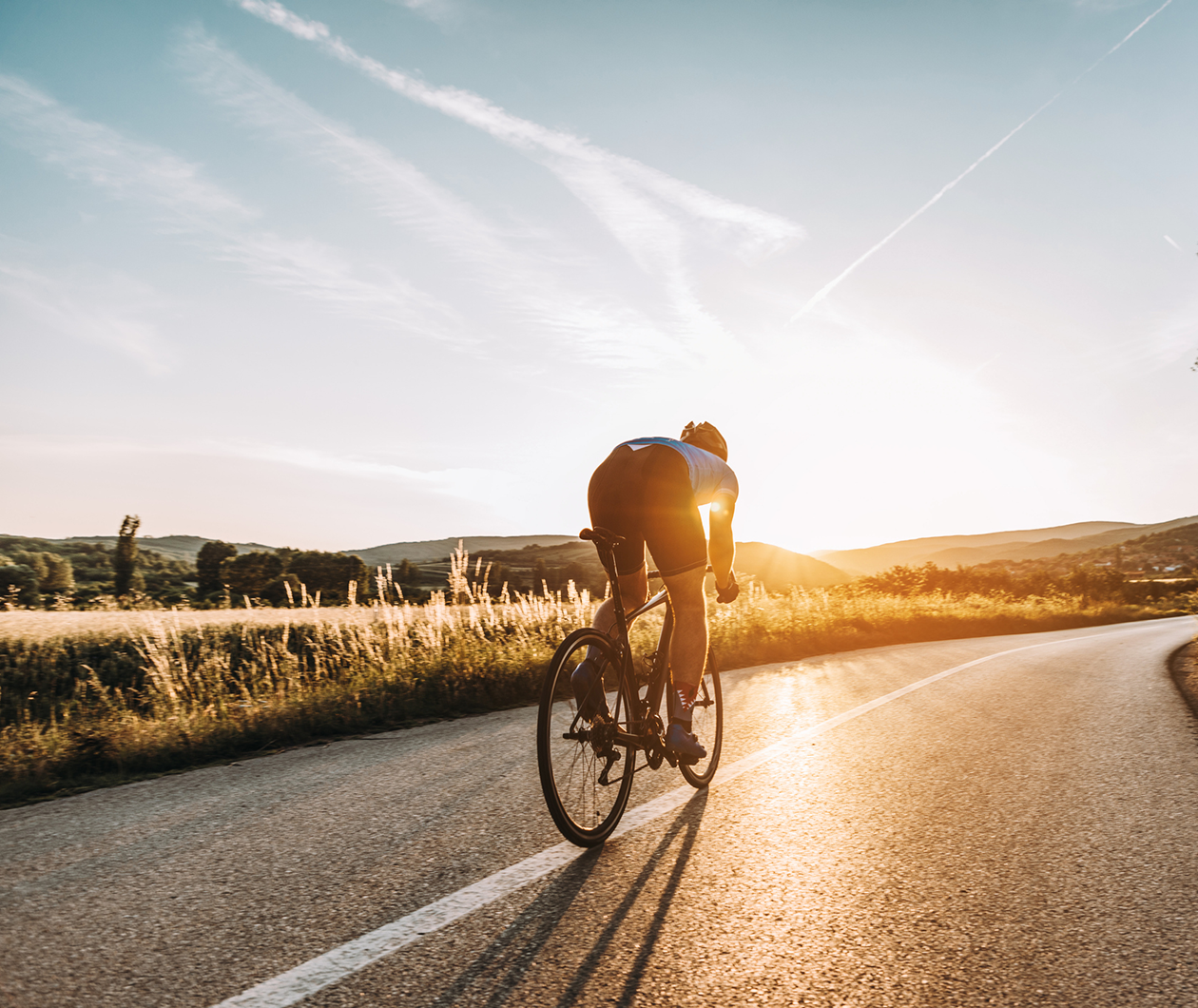 Fahrradfahrer faehrt auf einer leeren Straße bei Sonnenuntergang